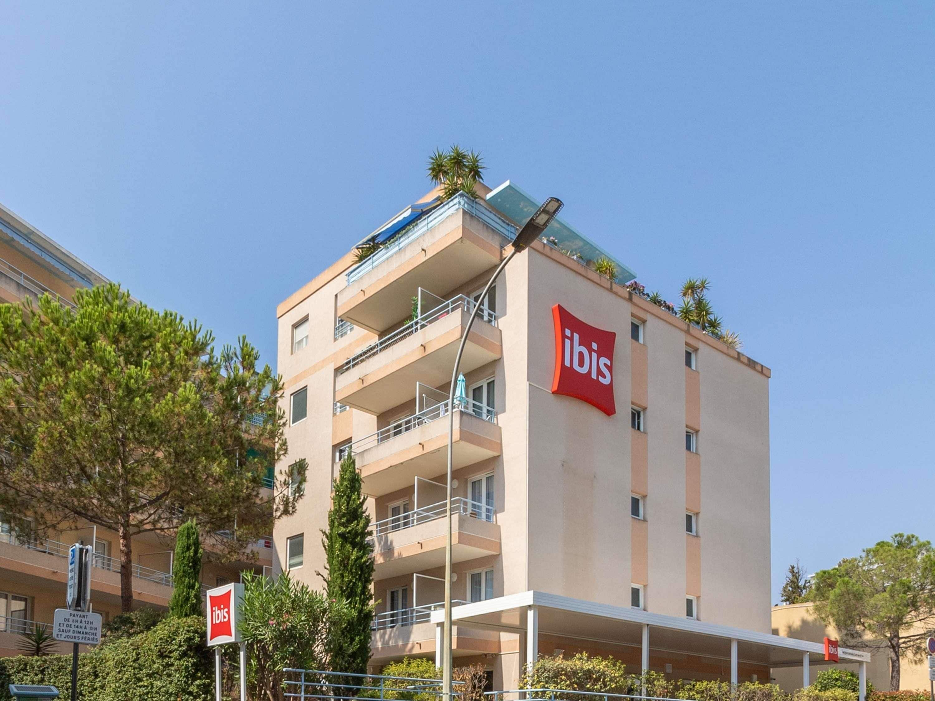 Ein mehrgeschossiges Gebäude mit einem gut sichtbaren 'ibis'-Schild, Balkonen und blauem Himmel.