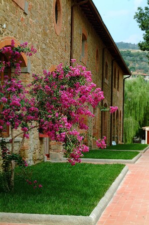 A stone building with a brick facade, a well-maintained lawn, and a pathway leading to the entrance. - Agriturismo Antico Borgo Poggitazzi (Terranuova Bracciolini)