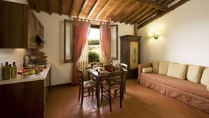 A rustic kitchen with wooden cabinets, a dining table set for two, and a sofa in a cozy corner. - Agriturismo Antico Borgo Poggitazzi (Terranuova Bracciolini)