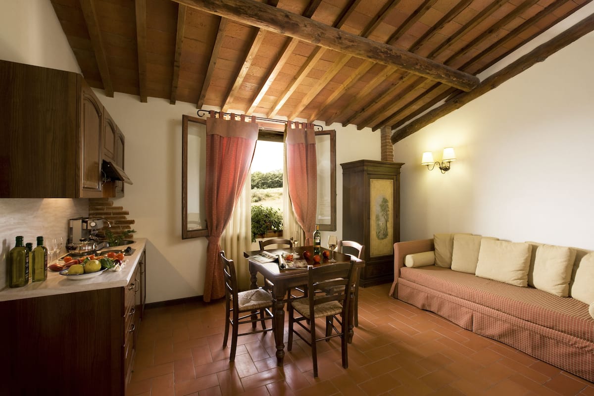 A rustic kitchen with wooden cabinets, a dining table set for two, and a sofa in a cozy corner.
