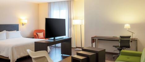 Una habitación de hotel con una cama, un escritorio con computadora, un televisor, un sofá verde y un sillón mecedora.