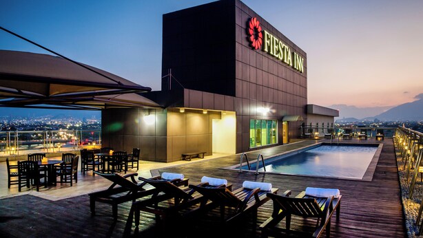 Un hotel moderno con zona de piscina, mobiliario exterior y vistas a la ciudad.