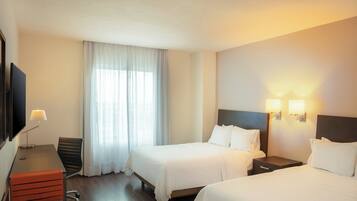A hotel room with two beds, a desk with a lamp, a chair, and a TV.