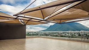 Una terraza amplia con vistas a la montaña y al paisaje urbano, con un diseño moderno que incluye vigas metálicas y toldos color beige.