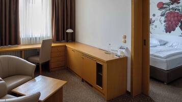 Una habitación de hotel con un escritorio de madera, una silla, una cama y un ventanal con cortinas.