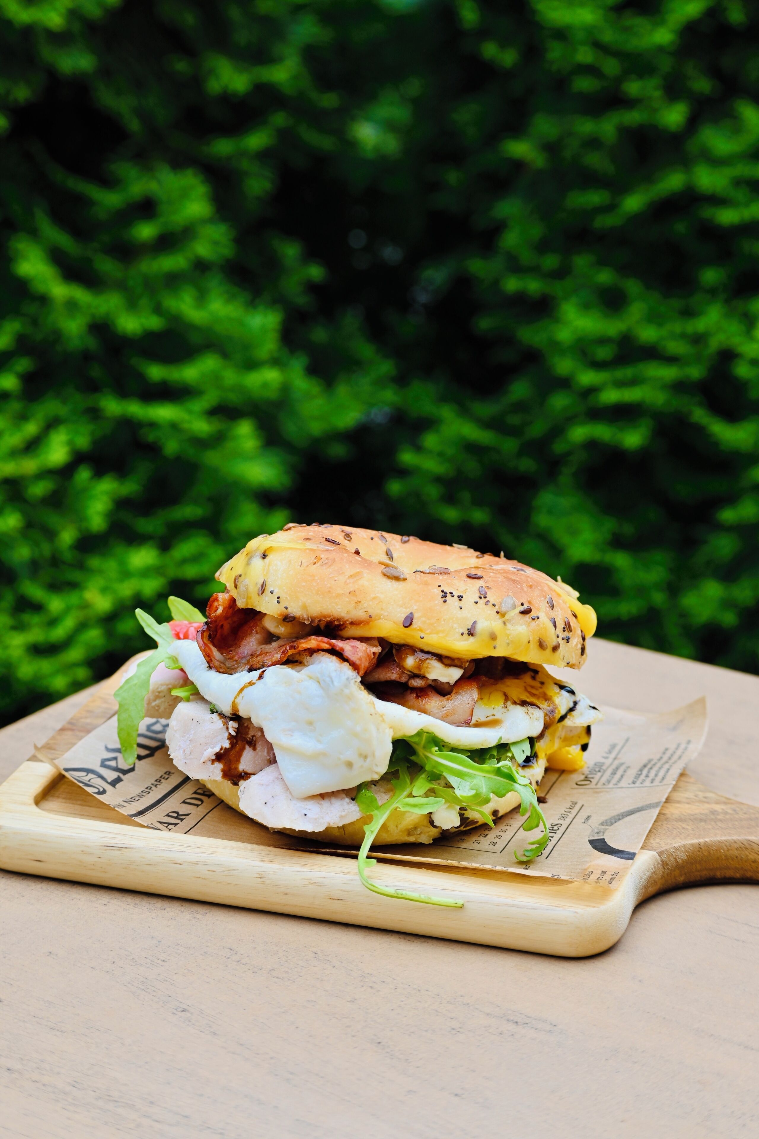 A sandwich on a wooden board with a green leafy background.