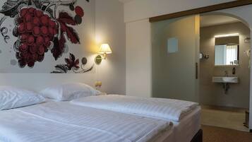 A hotel room with two beds, a wall-mounted lamp, a mirror, and a bathroom visible through an archway.