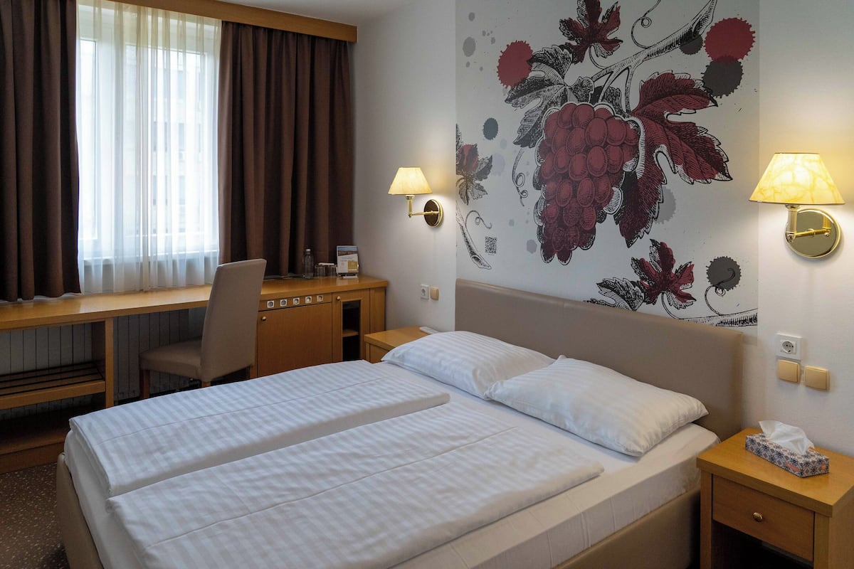 Ein Hotelzimmer mit zwei Betten, einem Schreibtisch, einem Stuhl und einer Wand mit floralem Wandbild.