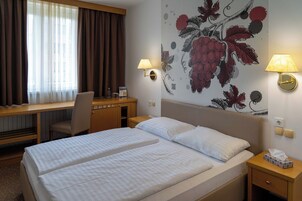 A hotel room with two beds, a desk, a chair, and a wall with a floral mural.