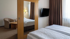 Ein Hotelzimmer mit einem Bett, einem Schreibtisch, einem Sessel, einem Fernseher und einem Spiegel.