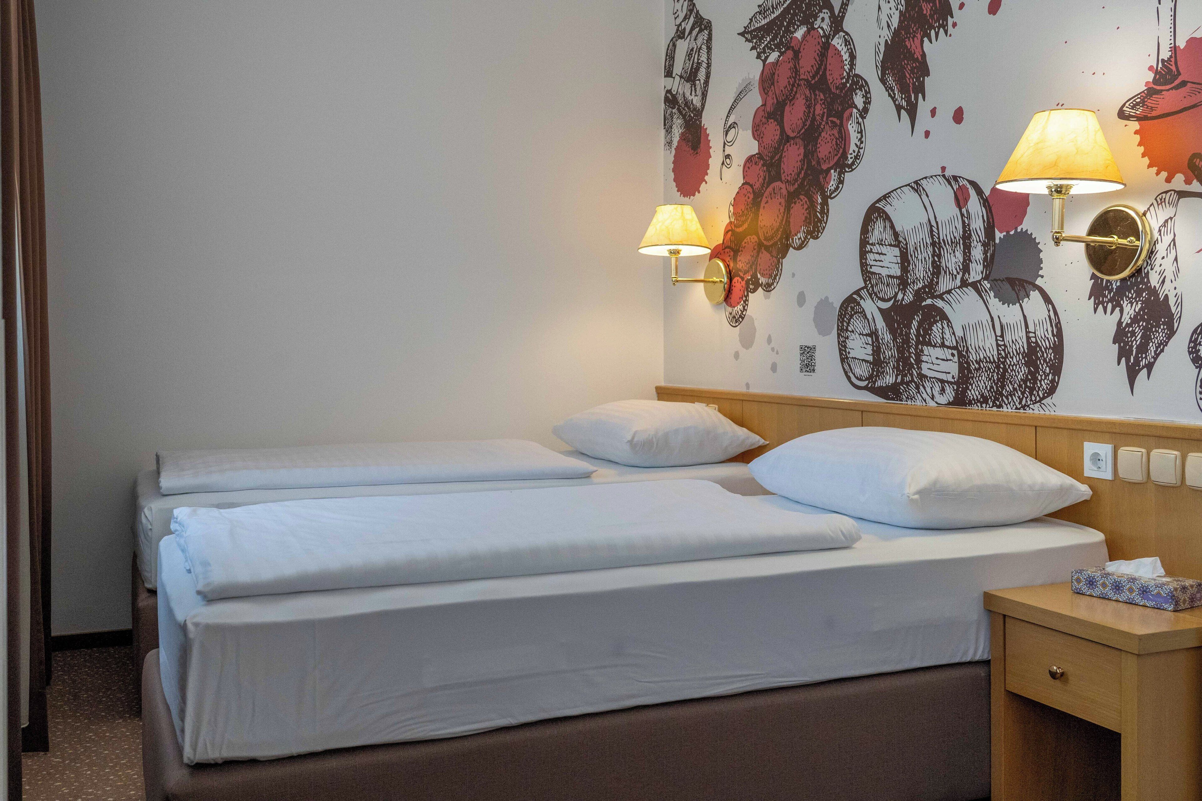 A hotel room with two beds, a wooden headboard, a nightstand with a lamp, and a wall mural.