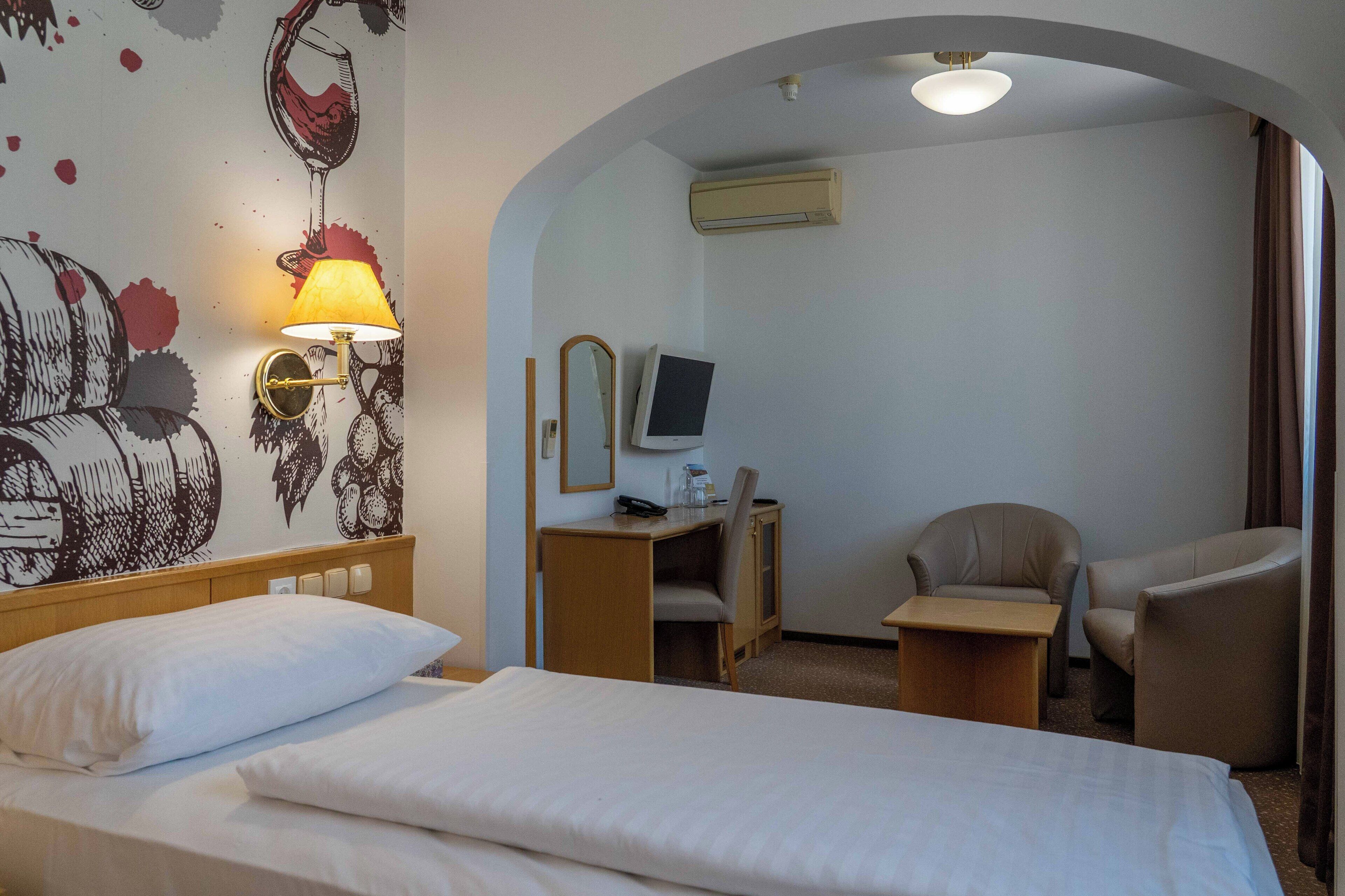 A hotel room with a bed, a desk with a chair, a TV, and a lamp.