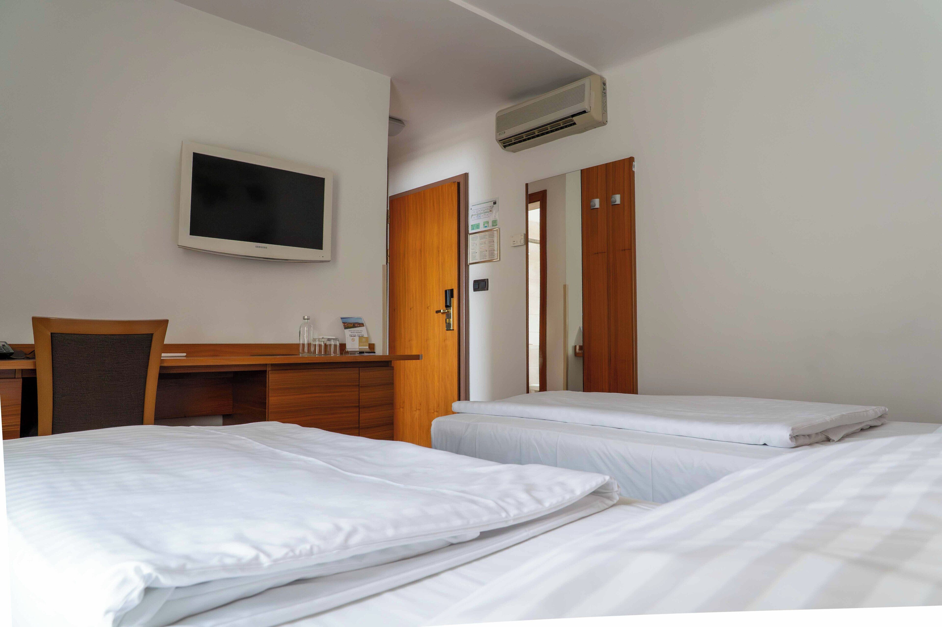 A hotel room with two beds, a desk, and a television.