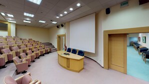 Ein Konferenzraum mit Stufenreihen, einem Rednerpult und einer Projektionsleinwand.