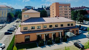 Ein mehrstöckiges Gebäude mit flachem Dach, zahlreichen Fenstern und einem Parkplatz mit Autos.