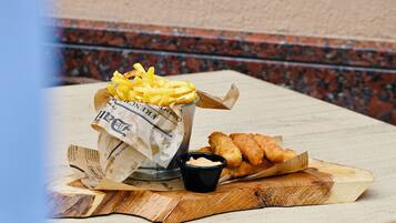 A meal of French fries, breaded fish, and dipping sauces on a wooden board.