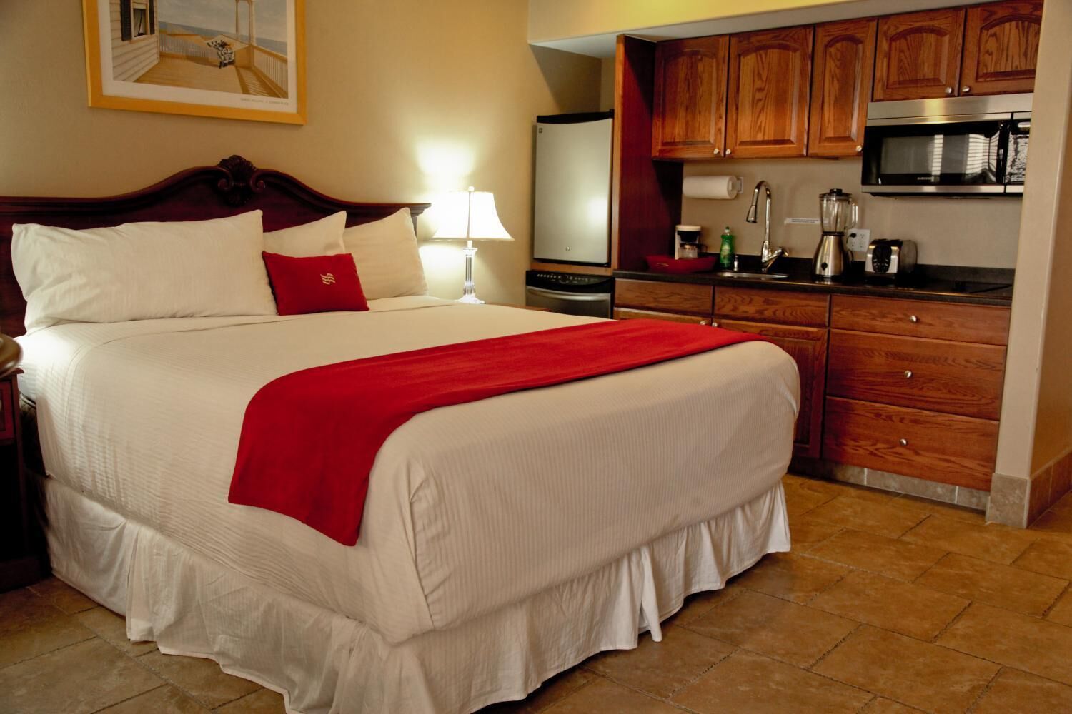 A hotel room with a large bed, a red throw blanket, wooden cabinets, a microwave, and a refrigerator.