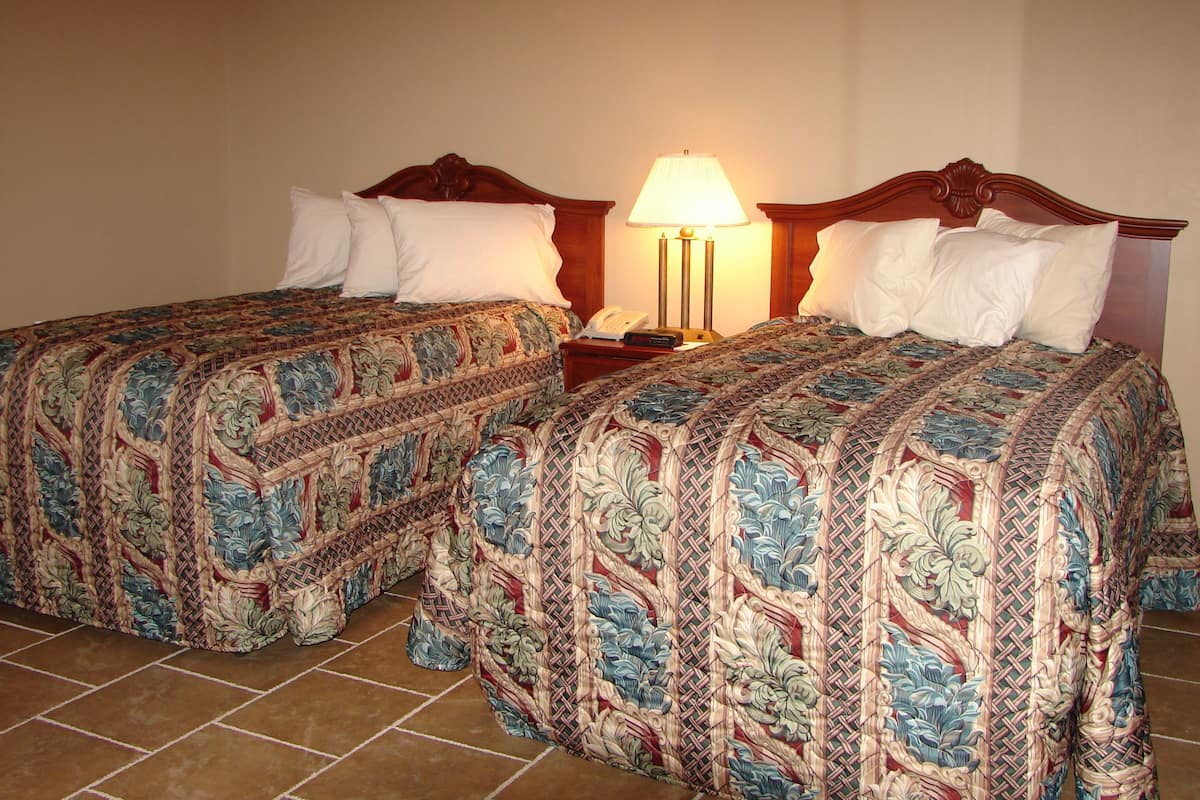 A hotel room with two beds, each with a floral-patterned bedspread, a nightstand with a lamp, and a telephone.