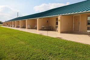 A row of single-story motel rooms with individual tables and chairs, a covered outdoor area, and a grassy lawn. - Lake Grassy Inn & Suites (Lake Placid)