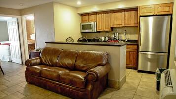 Ein Wohnzimmer mit braunem Ledersofa, eine Küche mit Holzausstattung, einem Edelstahlkühlschrank und einer Mikrowelle.