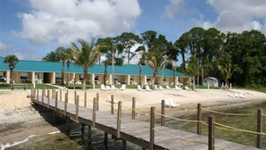 Un hôtel situé en bord de mer, avec une promenade en bois menant à une plage de sable où se trouvent des chaises longues.