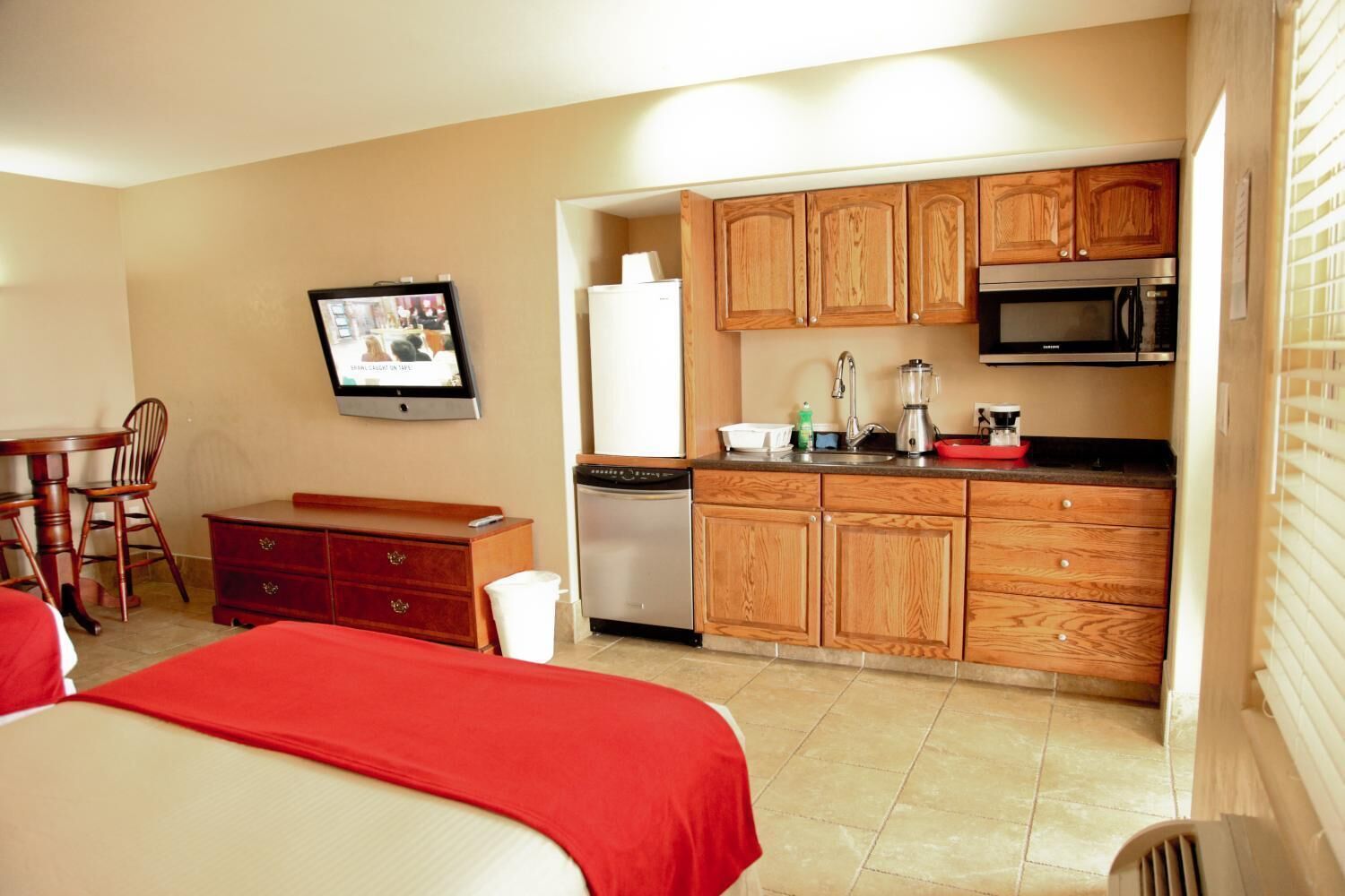 A compact hotel room with a kitchenette, a dining area, and a TV.