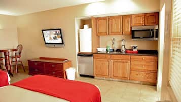 A compact hotel room with a kitchenette, a dining area, and a TV.