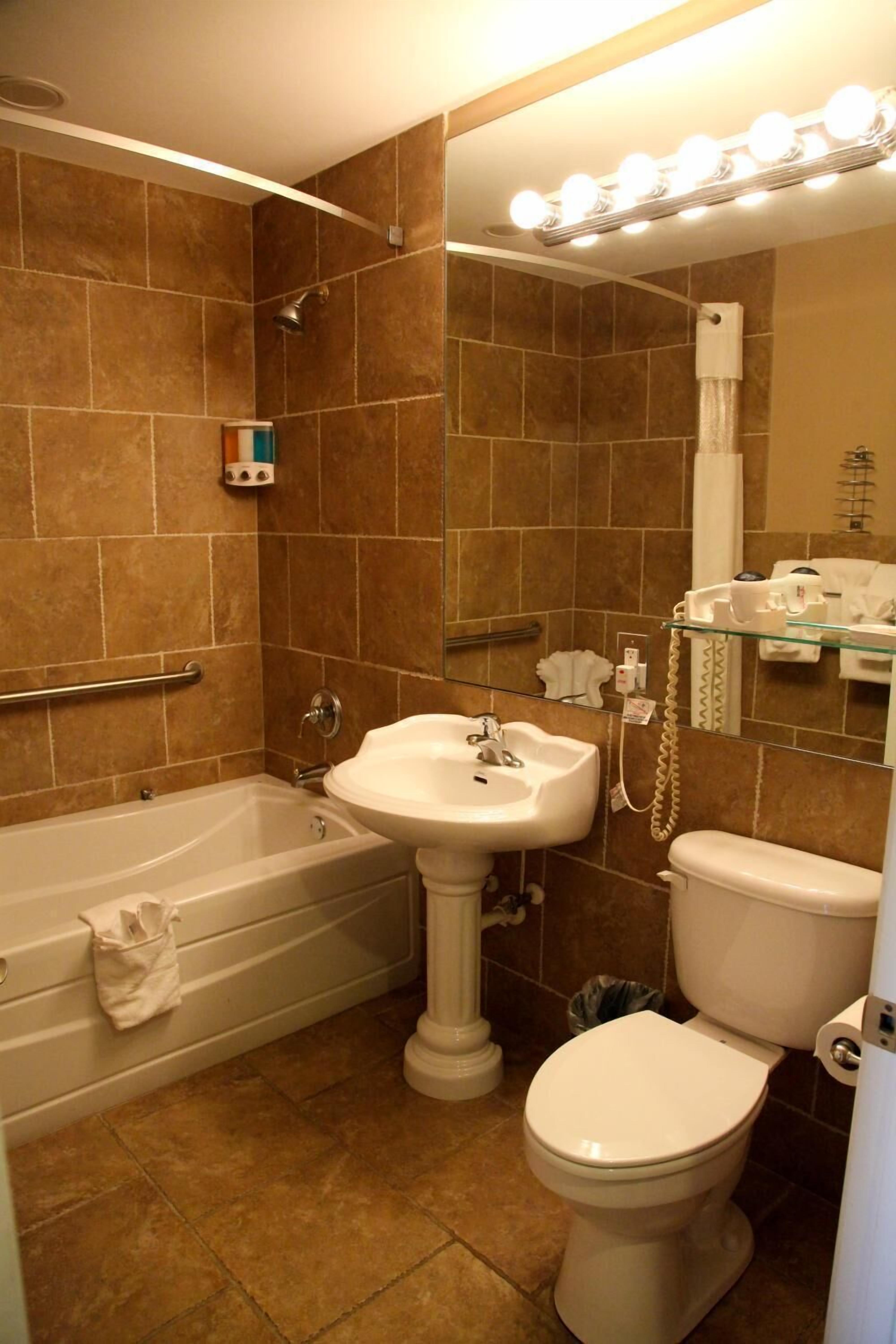 A bathroom with a bathtub, sink, toilet, and a vanity mirror with lights.