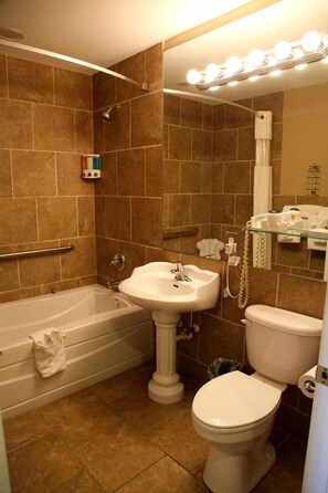 A bathroom with a bathtub, sink, toilet, and a vanity mirror with lights. - Lake Grassy Inn & Suites (Lake Placid)