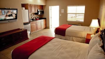 Een hotelkamer met twee bedden, een kitchenette, een televisie en een raam.