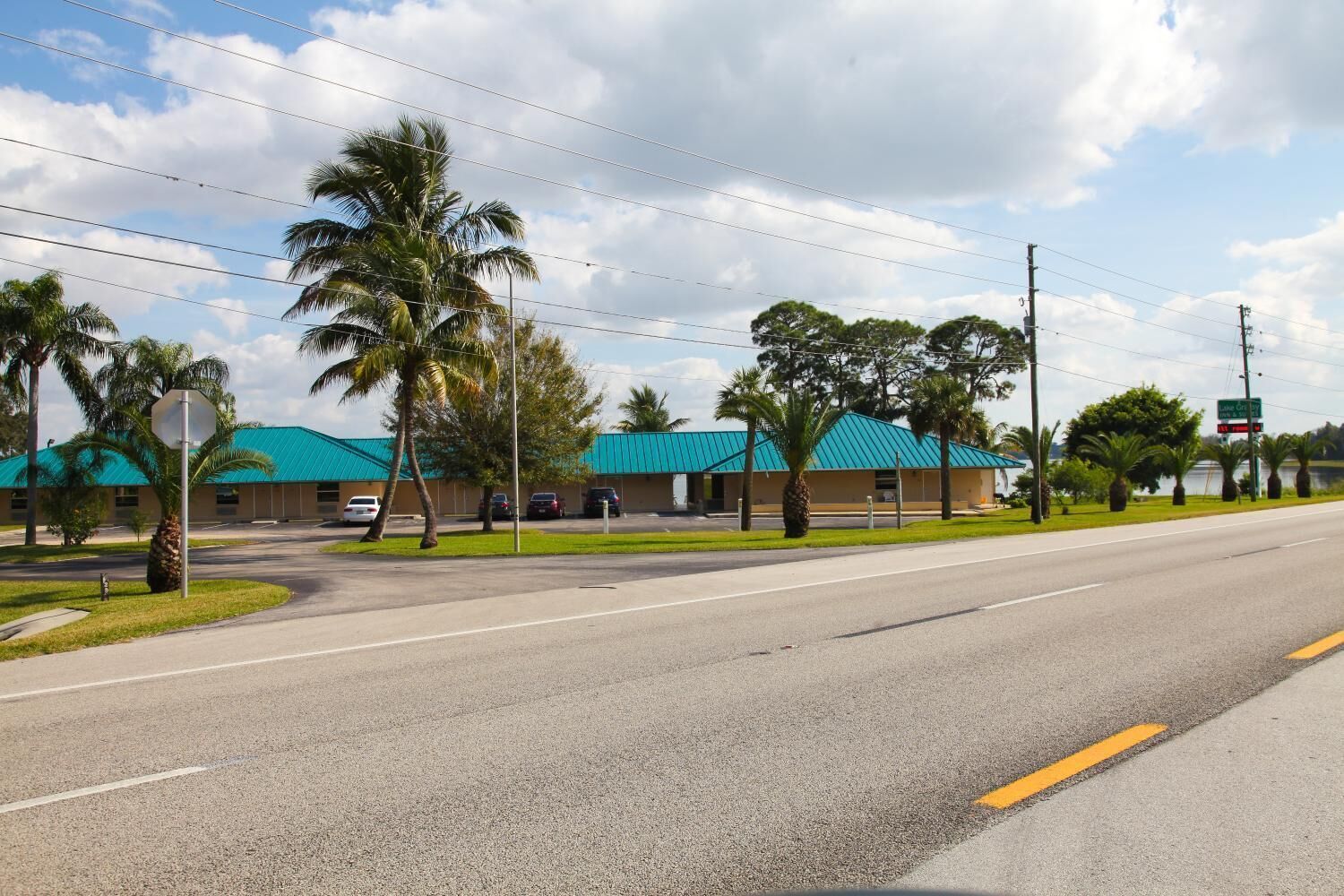 A motel with a green roof, palm trees, and a clear sky.