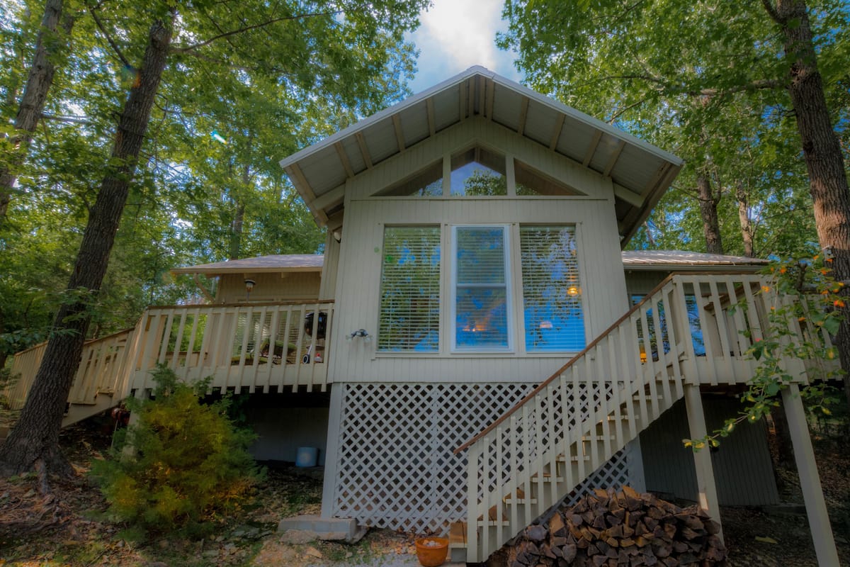 A cabin with a covered porch, a staircase, and a view of the surrounding forest.