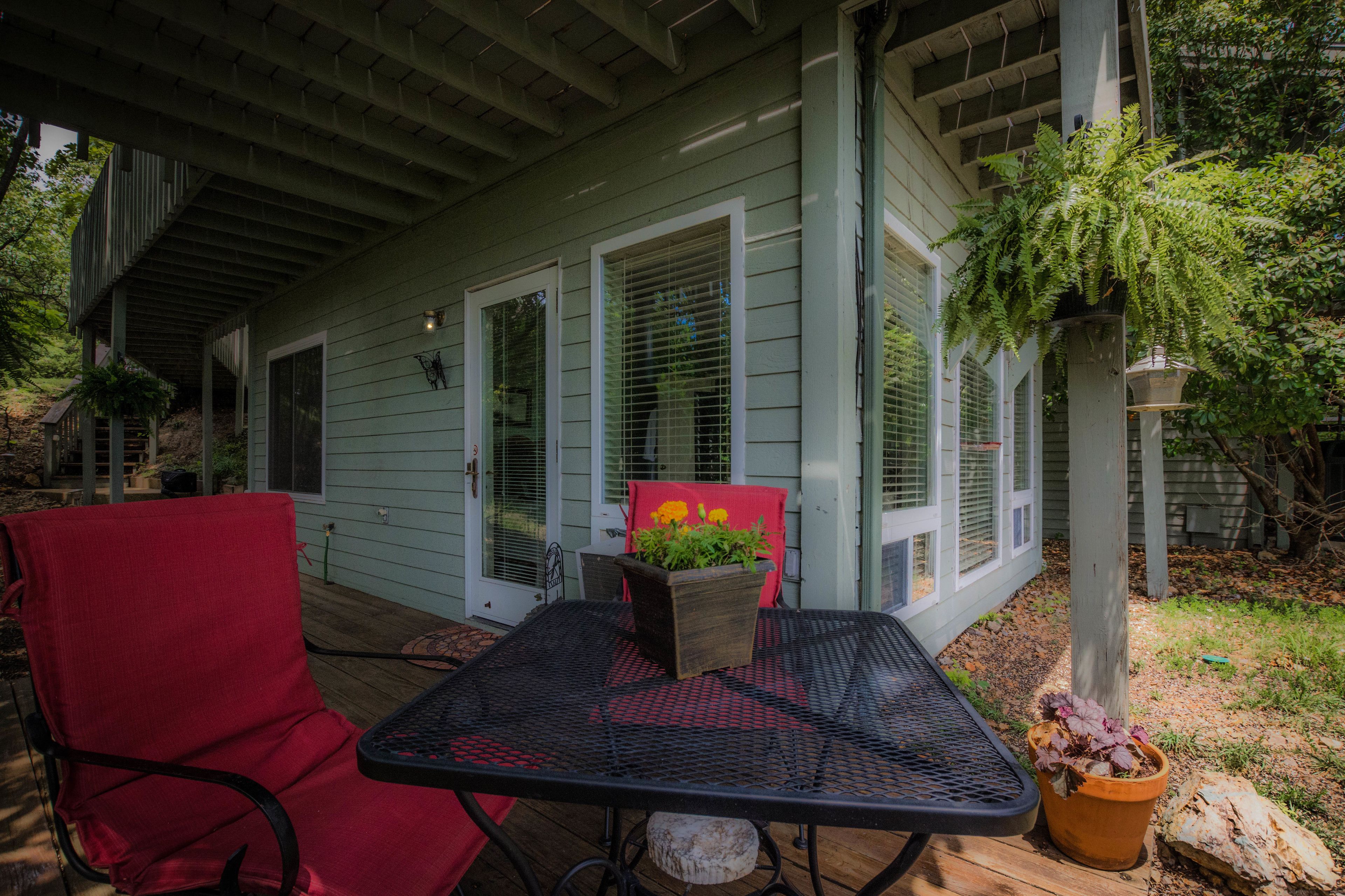 A covered patio with a metal table and red chair, a potted plant, and a wooden deck.