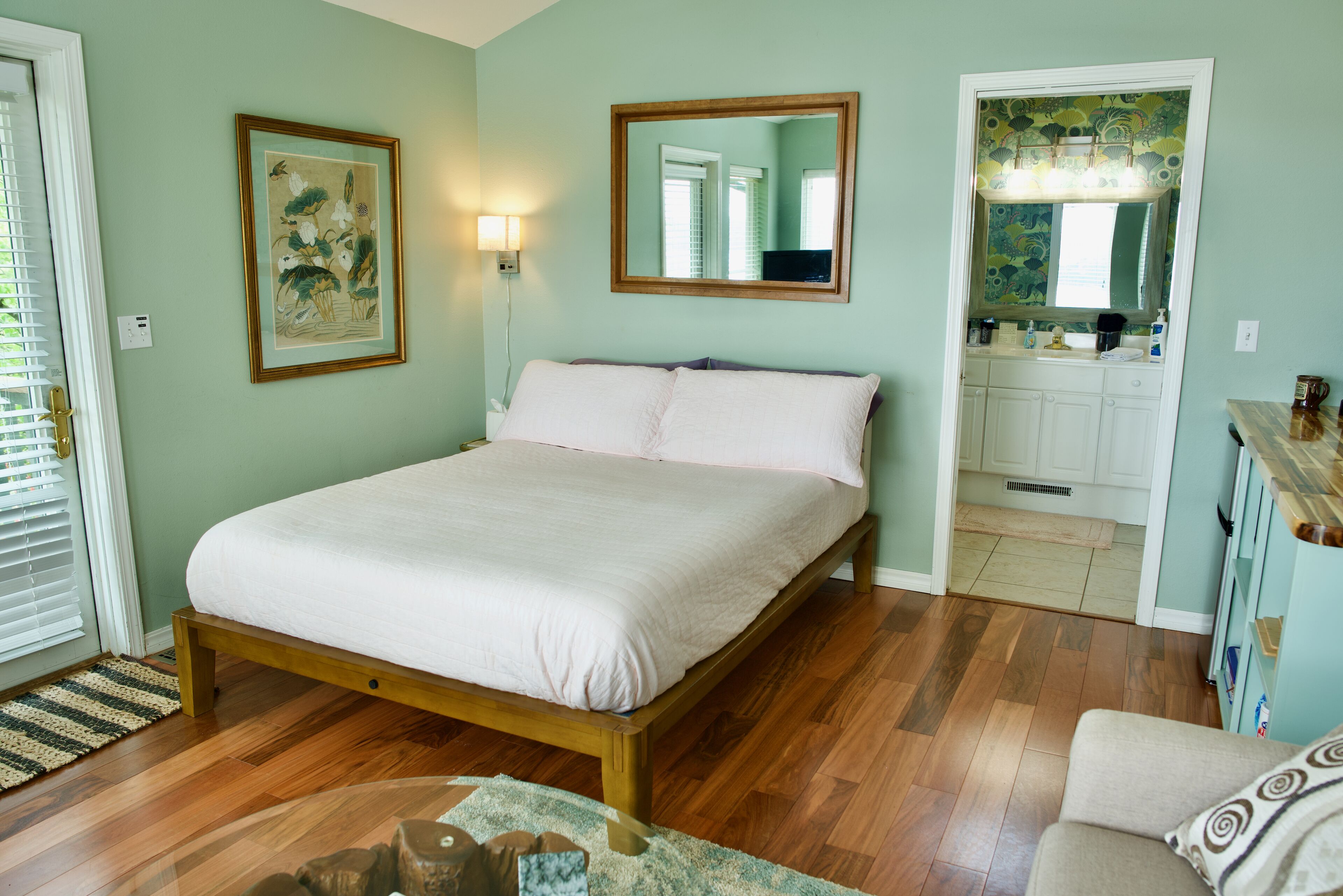 A bedroom with a bed, a wooden floor, a door leading to a bathroom, and a framed picture on the wall.