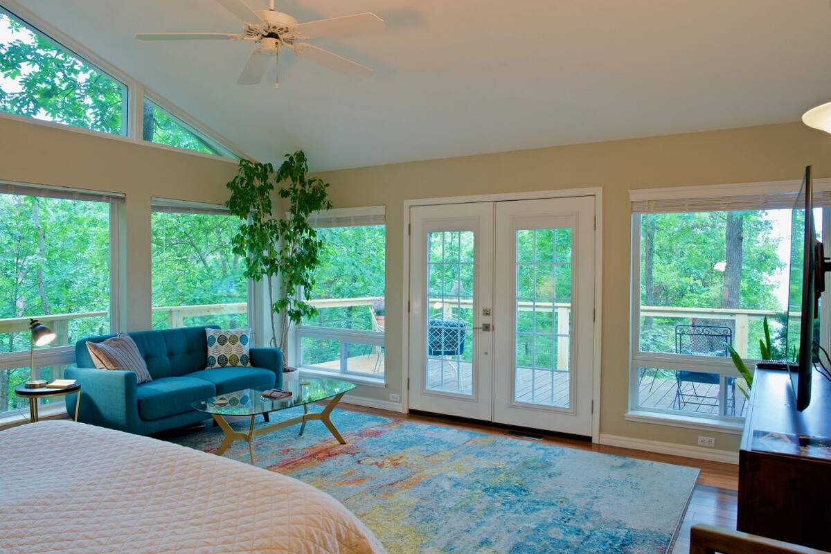 A spacious bedroom with a large bed, a blue sofa, a coffee table, and a view of the outdoors through large windows and sliding doors.