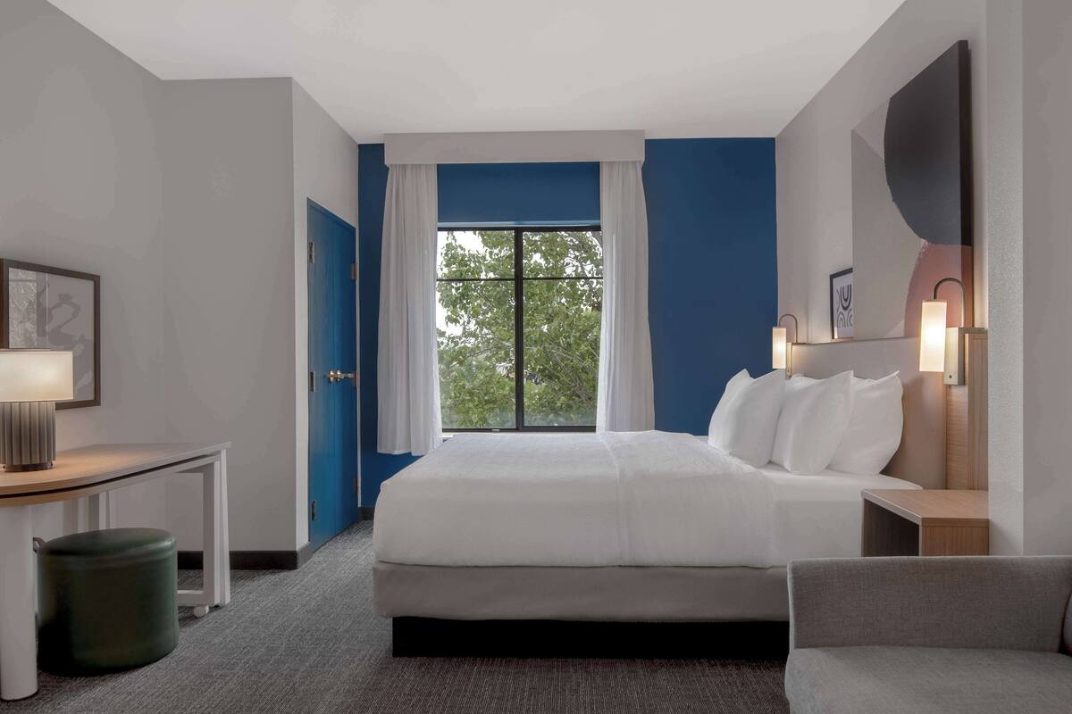 A hotel room with a large bed, a desk, a chair, and a window with curtains.