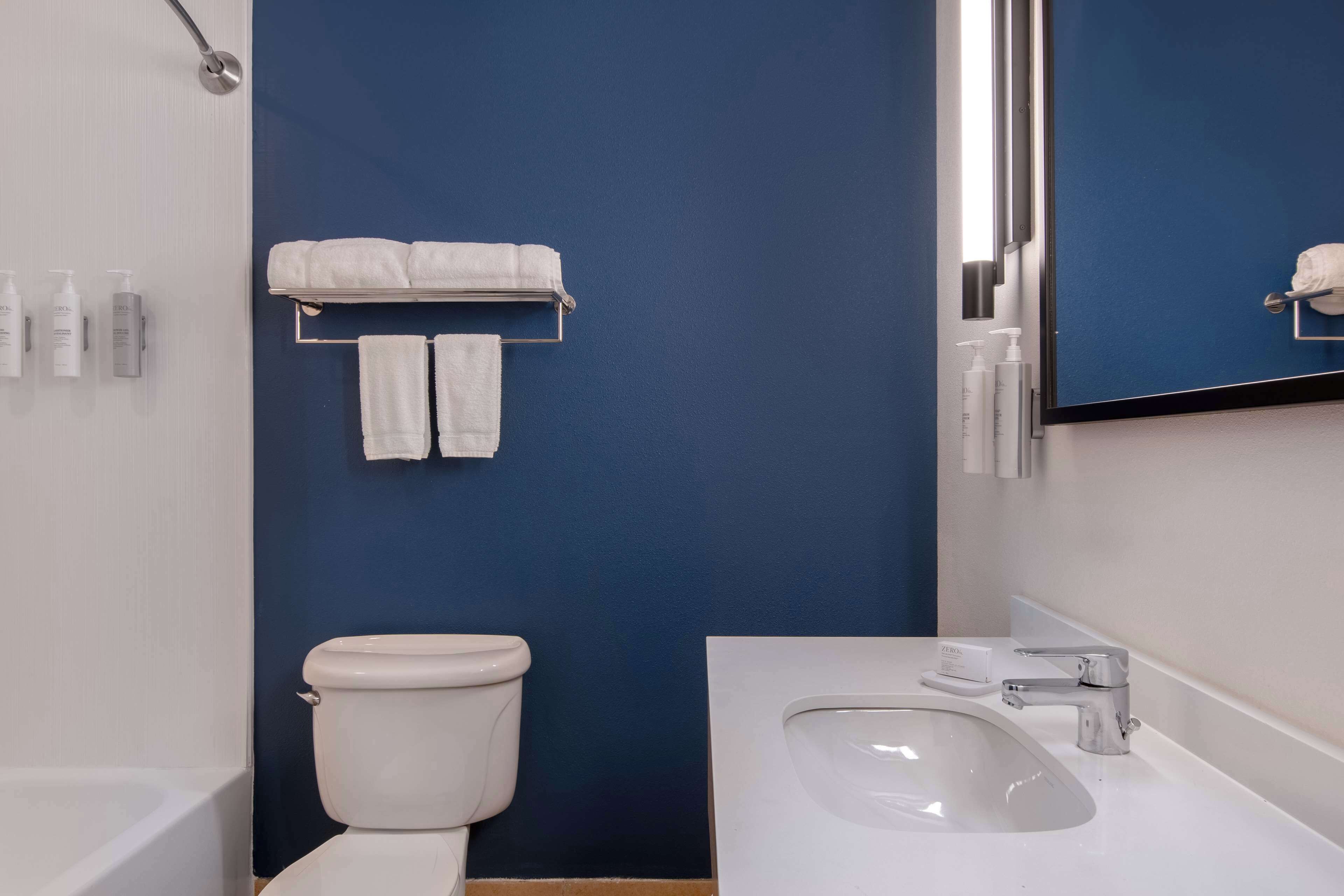 A bathroom with a white sink, a mirror, and a toilet against a blue wall.