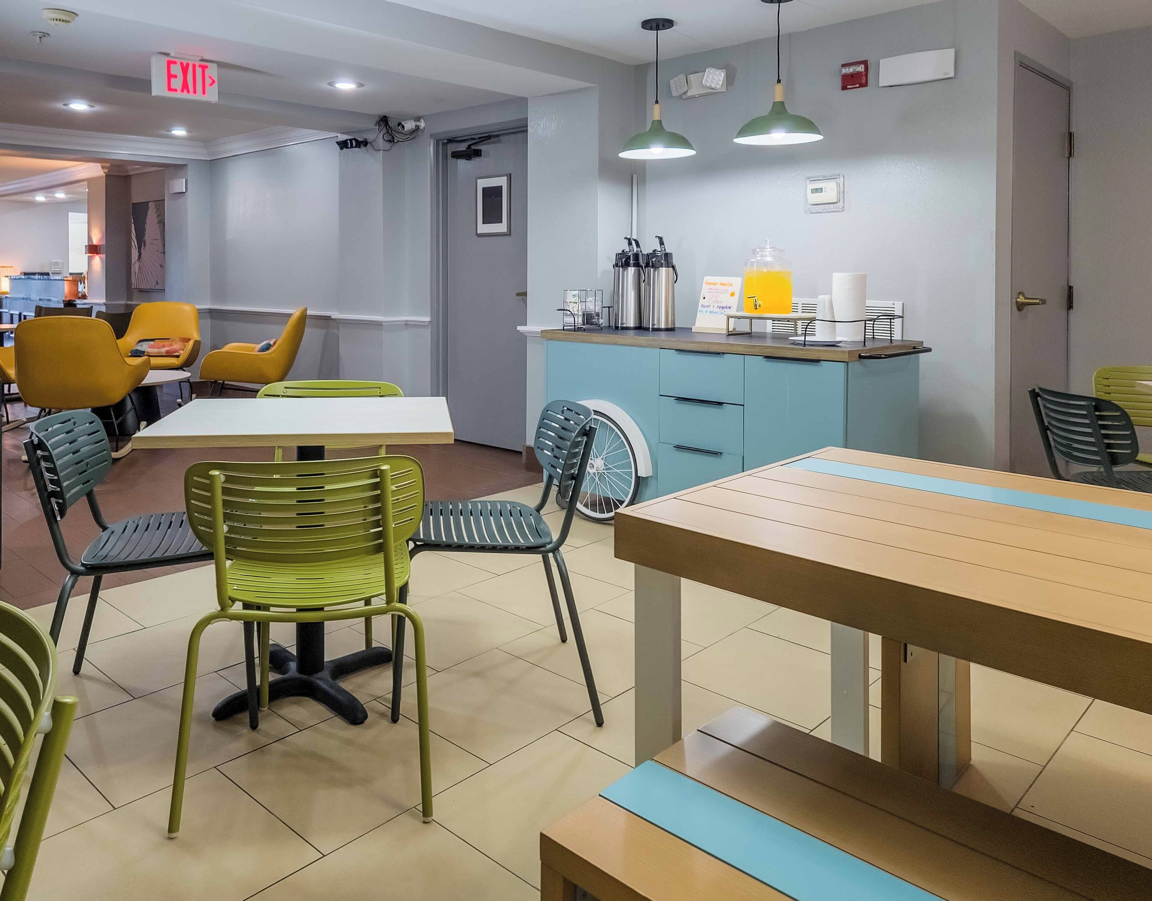 A dining area with tables and chairs, a counter with a coffee machine, and an exit sign.
