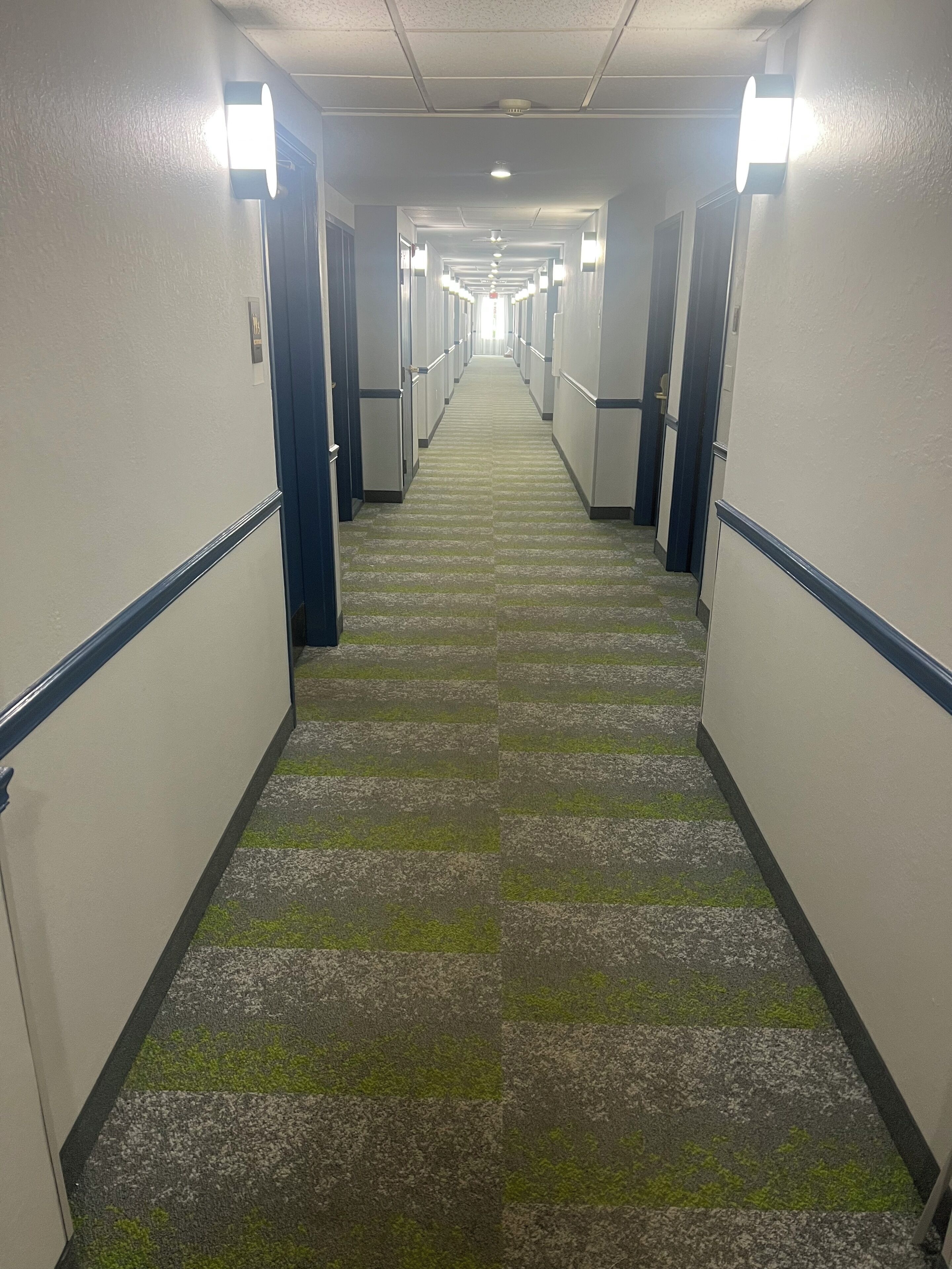 Ein langer, schmaler Hotelgang mit Teppichböden und Türen an beiden Seiten.