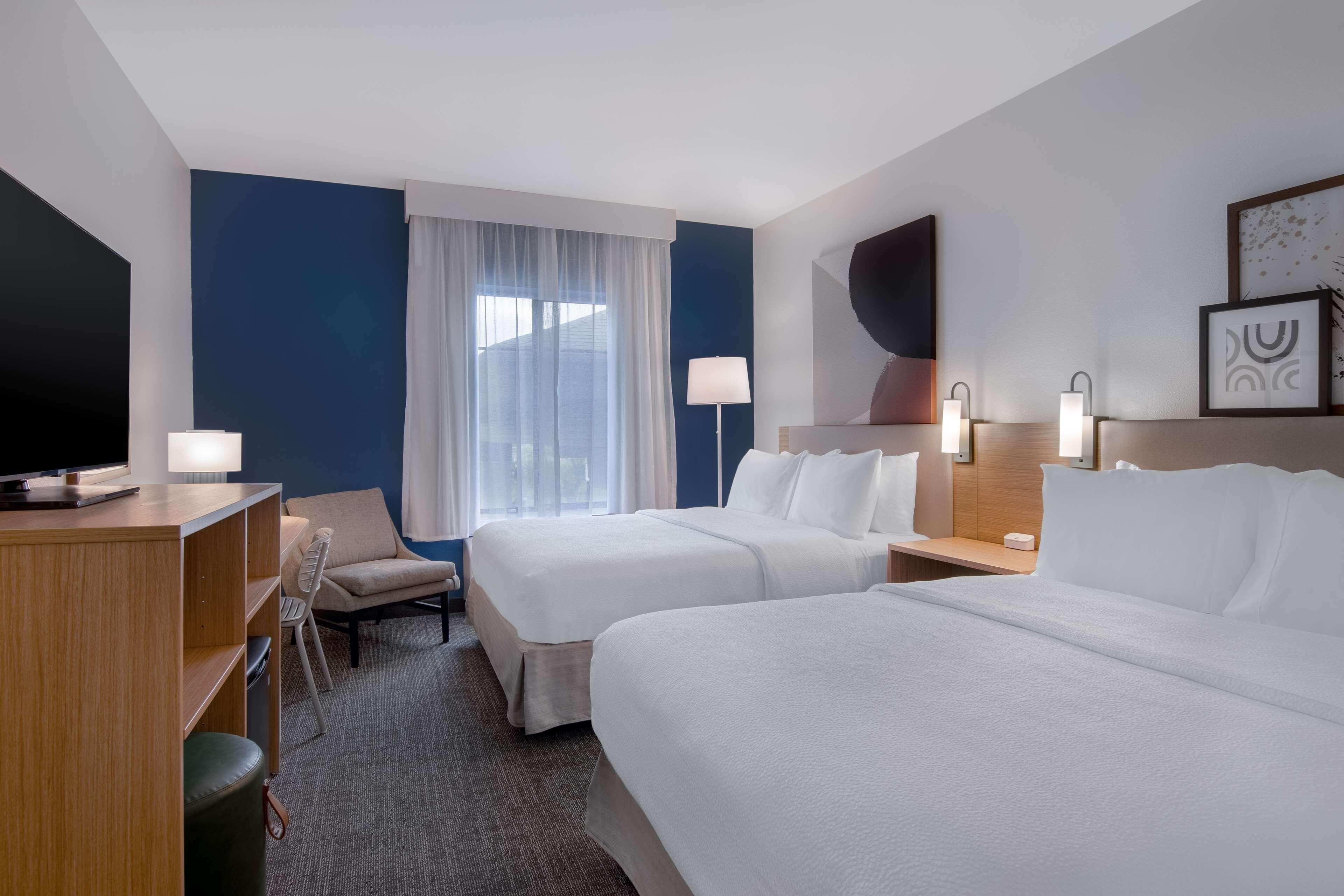 Habitación de hotel con dos camas, un escritorio, una silla, un televisor y una ventana con cortinas.