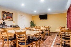 A dining area with wooden tables and chairs, a painting on the wall, a television, and a door.