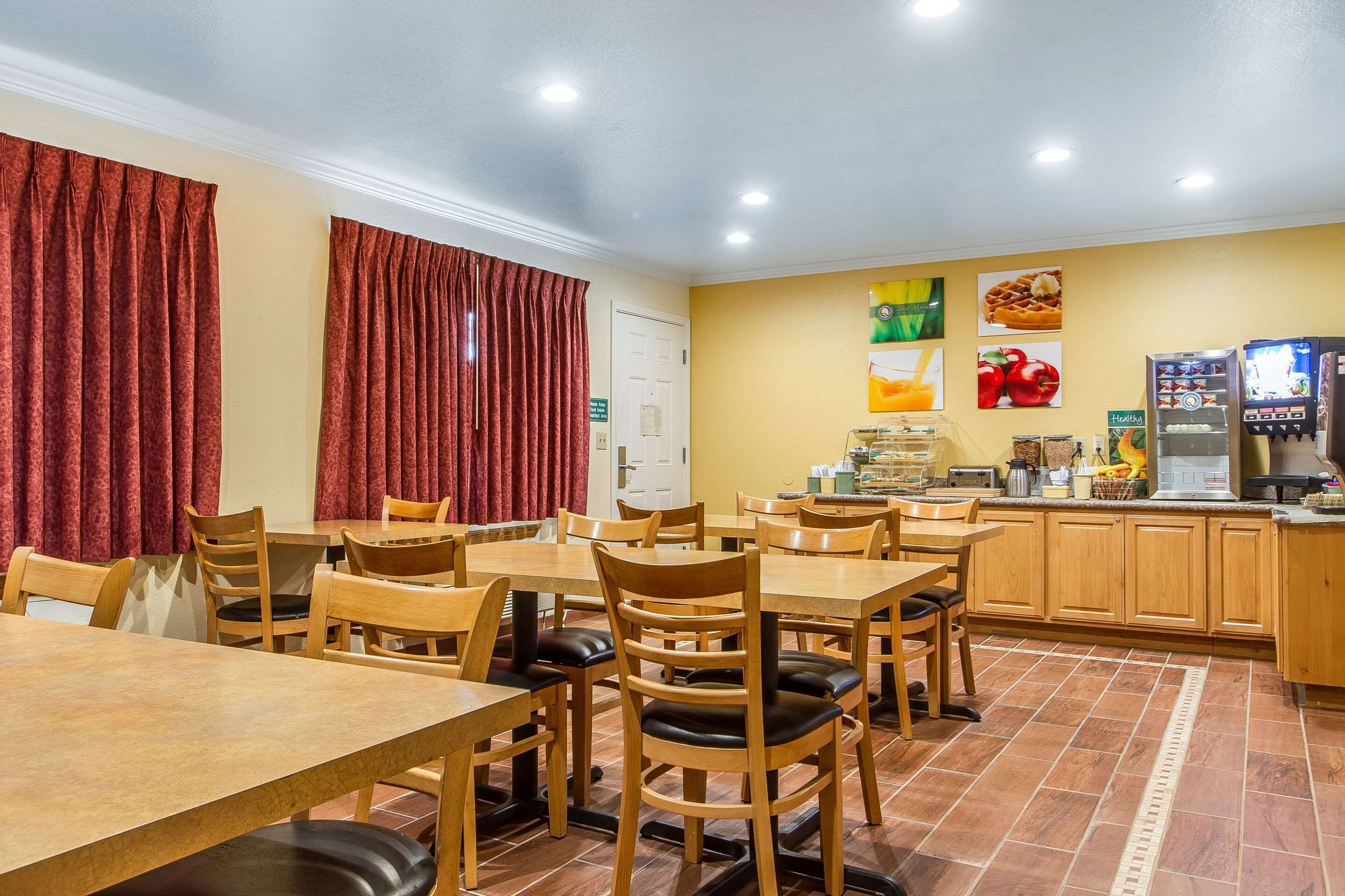 A dining area with wooden tables and chairs, a kitchen area with a coffee machine, and a counter with various food items.