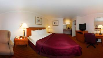 Habitación de hotel con cama, escritorio con computadora, silla, televisor y dos lámparas.