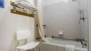 A bathroom with a bathtub, shower, and a white chair.