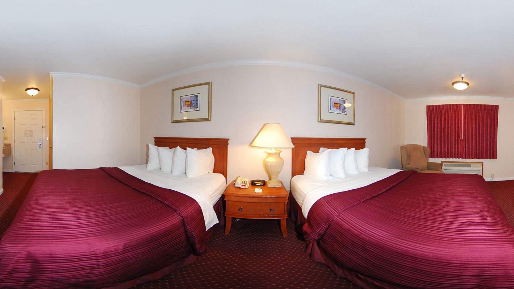 A hotel room with two beds, a nightstand with a lamp, and a red curtain.