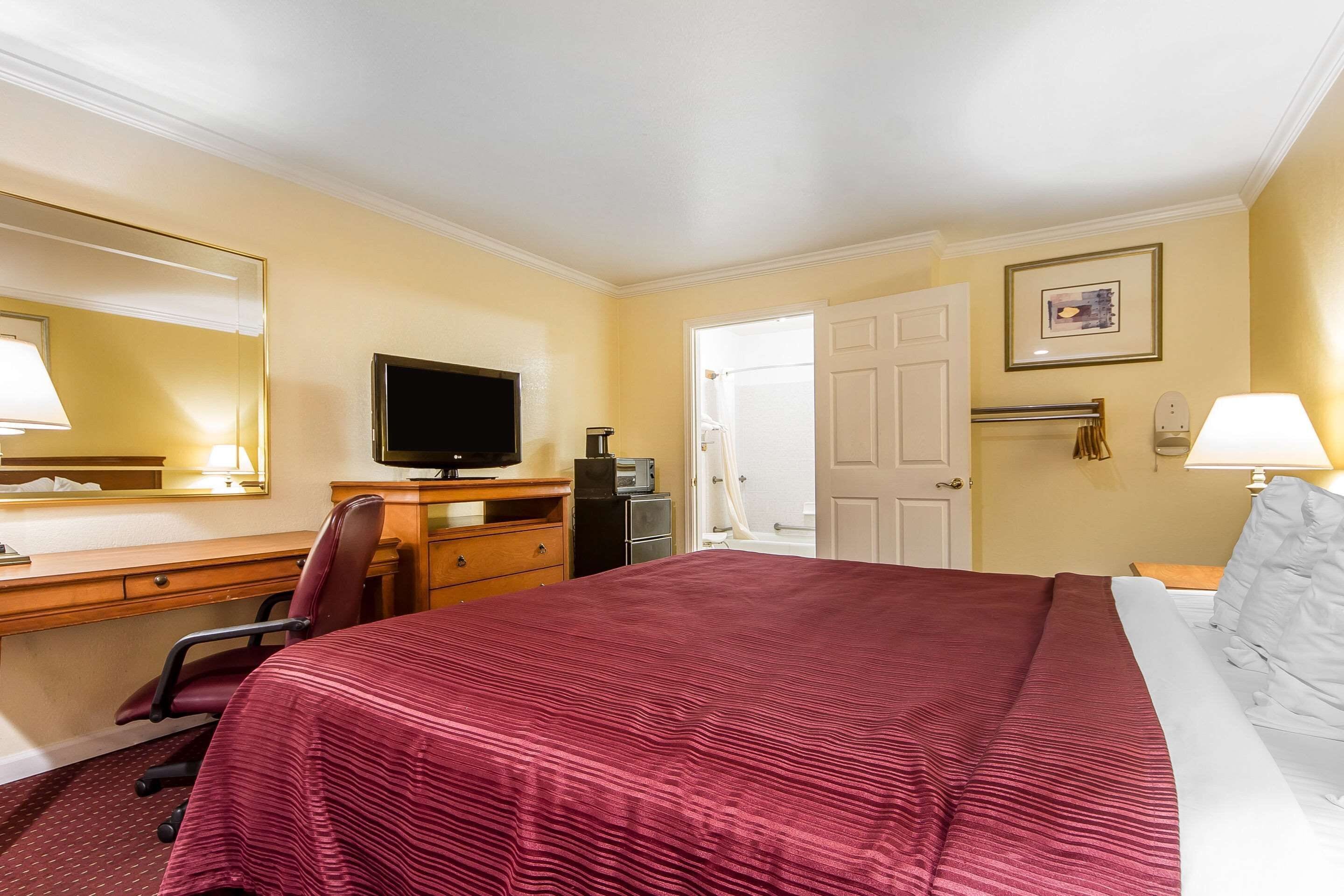 Une chambre d’hôtel avec un grand lit, un bureau avec un ordinateur, une télévision et une porte donnant sur une salle de bain.
