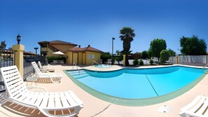 A swimming pool with lounge chairs, a hot tub, and a building with a yellow facade.