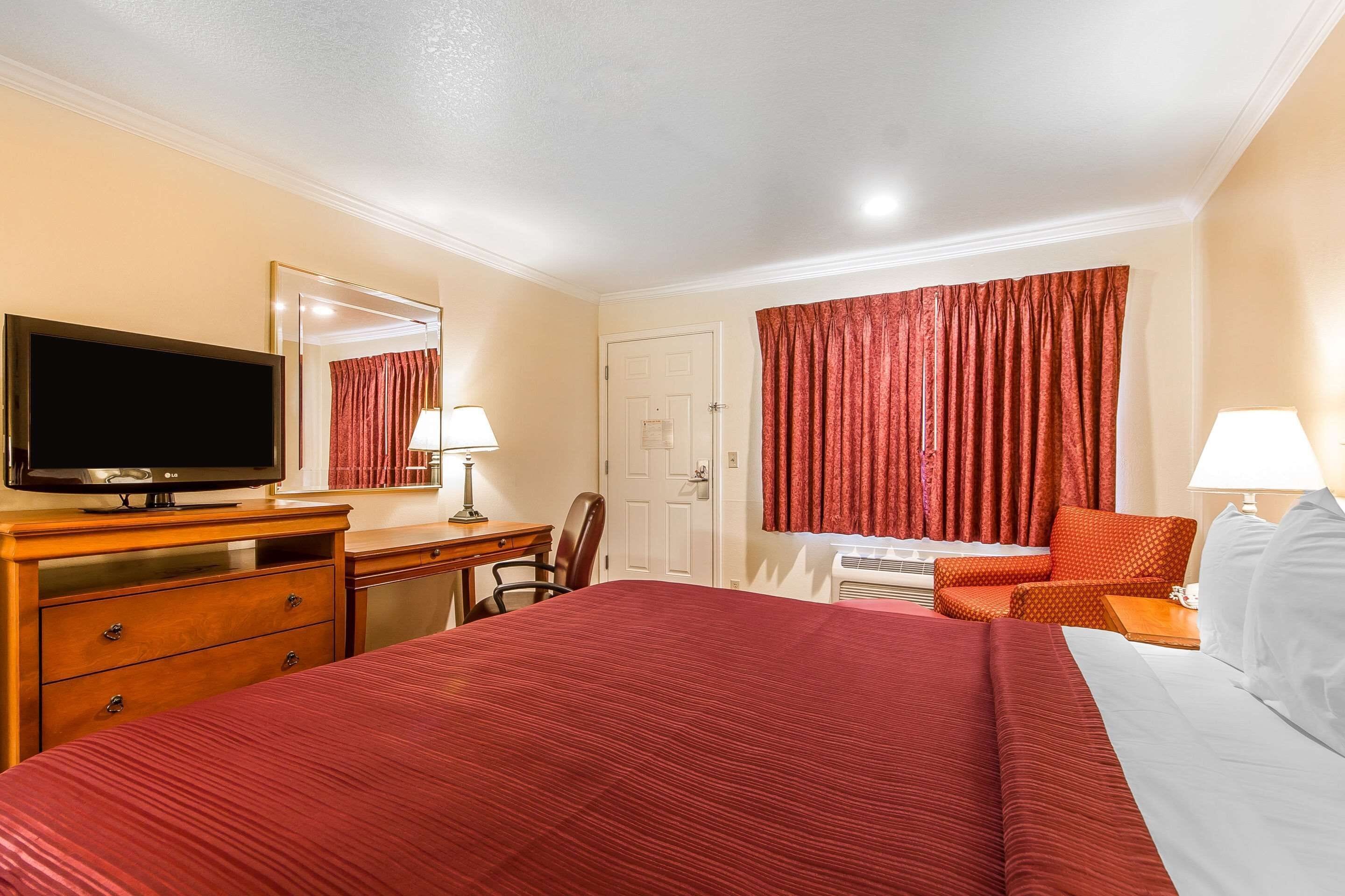 A hotel room with a large bed, a desk with a television, a chair, and a window with curtains.