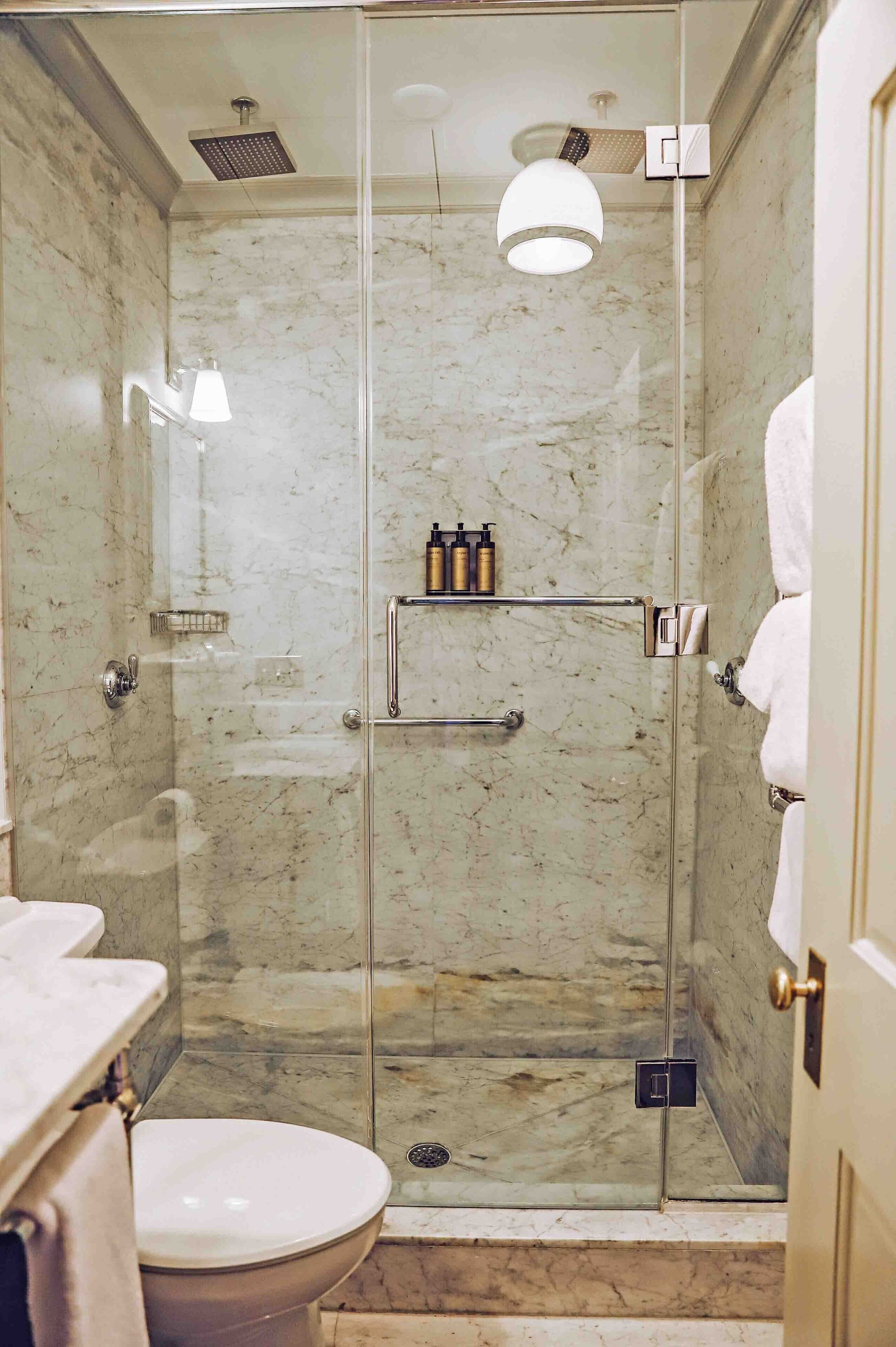 A modern bathroom with a glass-enclosed shower, marble walls, a toilet, and a sink.