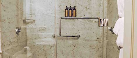 A modern bathroom with a glass-enclosed shower, marble walls, a toilet, and a sink.